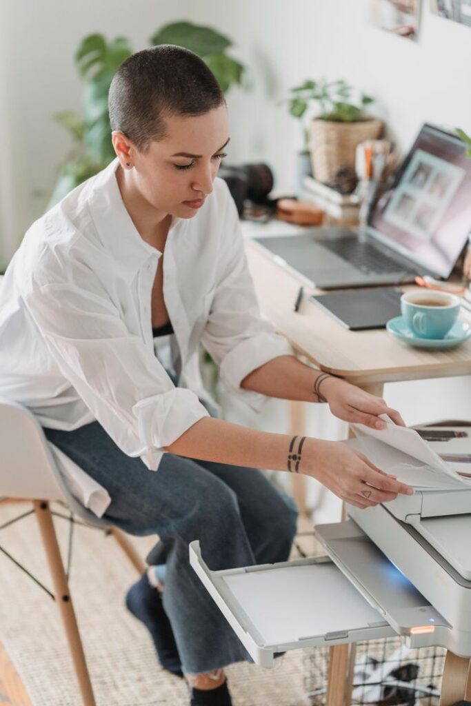 High angle of serious female photographer sitting in armchair and taking paper for printing photos