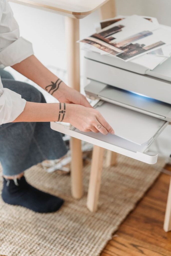 From above of crop anonymous female photographer with tattoo preparing paper for printing photos at home
